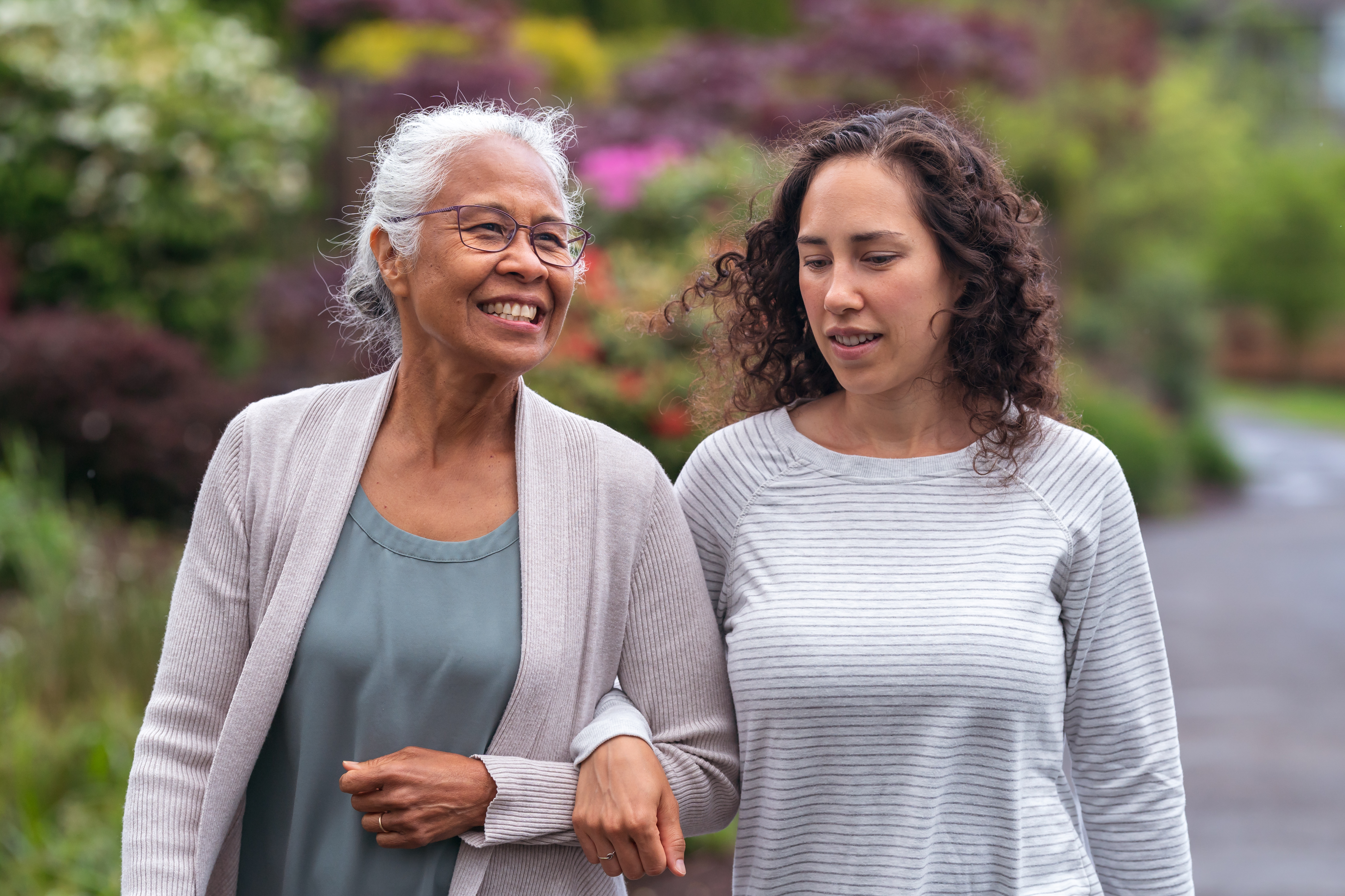 Two people walking side by side with linked arms through a garden.