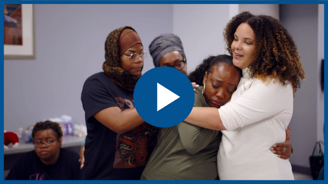 Doulas embracing during a training session. Play button for video. 