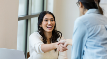 Women sitting at desk with laptop shakes hand client.