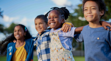 Group of four children linking arms outside. 